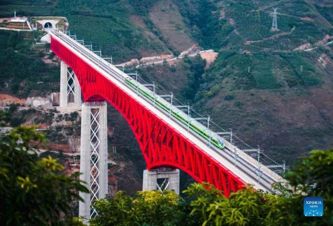 Vlak s několika elektrickými lokomotivami na železnici z Číny do Laosu přejíždí po velikém mostě přes řeku Yuanjiang v jihozápadní čínské provincii Yunnan 3. prosince 2021. Železnice mezi Čínou a Laosem bývala vlajkovou lodí mezi projekty Iniciativy pásu a cesty. [Photo/Xinhua]