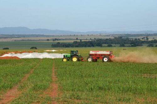 Traktor poblíž hromady kamenného prachu sprejuje pole na minerály bohatým kamenným prachem na farmě Vargem Dourada v Padre Bernardo v brazilském státě Goias, 19. května 2022. (Evaristo Sa/AFP via Getty Images)