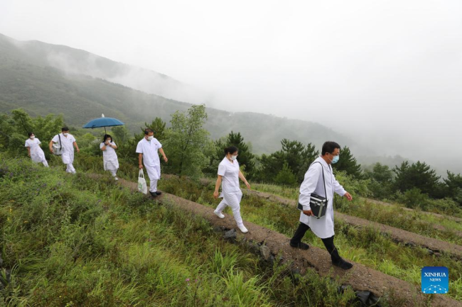 Ο Γουάνγκ Τζινχούι (πρώτος δεξιά) και οι συνάδελφοί του περπατούν σε έναν ορεινό δρόμο τον Ιούλιο του 2020. (Xinhua)