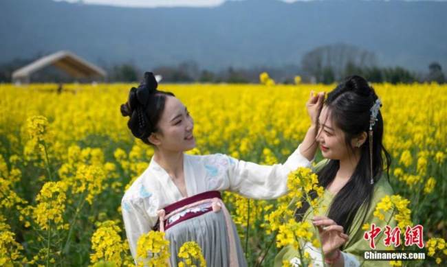 Δυο νεαρές γυναίκες με χάνφου, τις παραδοσιακές κινέζικες φορεσιές, βγάζουν φωτογραφίες σε ένα χωράφι με λουλούδια ελαιοκράμβης στη Χονγκγιά, στην επαρχία Σετσουάν της νοτιοδυτικής Κίνας, 1 Μαρτίου 2022. (Φωτογραφία: China News Service)