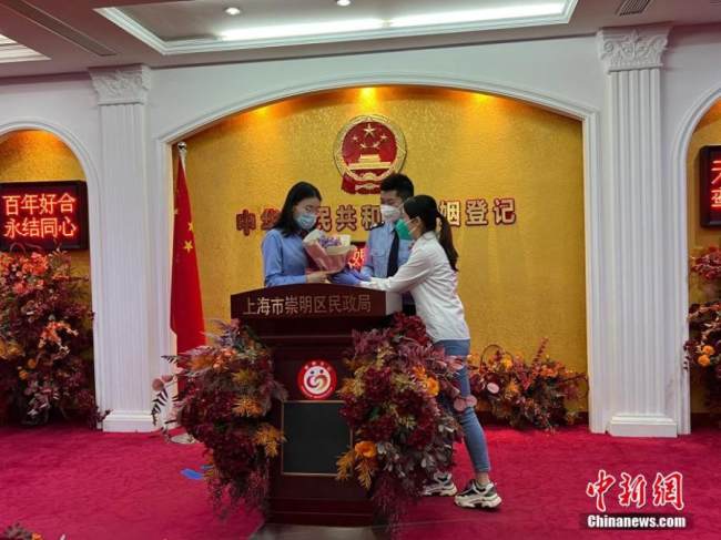 Ένα μέλος του προσωπικού προσφέρει ένα μπουκέτο λουλούδια καθώς και προϊόντα πρόληψης επιδημιών στους νεόνυμφους σε ένα κέντρο εγγραφής γάμων στην περιοχή Τσαομίνγκ, στη Σαγκάη της ανατολικής Κίνας, 20 Μαΐου 2022. (Φωτογραφία: China News Service) 